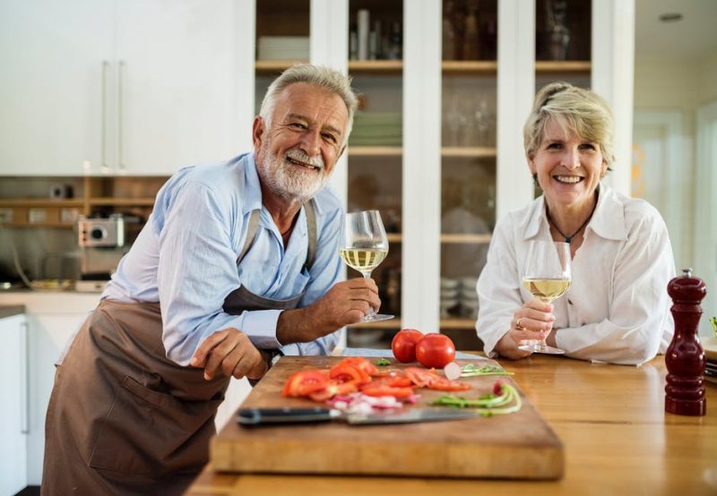 two senior citizens enjoying wine and cooking dinner at the kitchen island