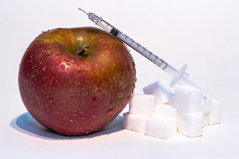 insulin syringe atop sugar cubes and an apple