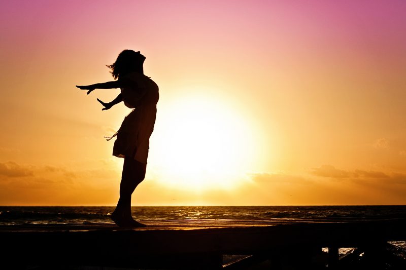 woman feeling free on a dock on ocean during sunrise