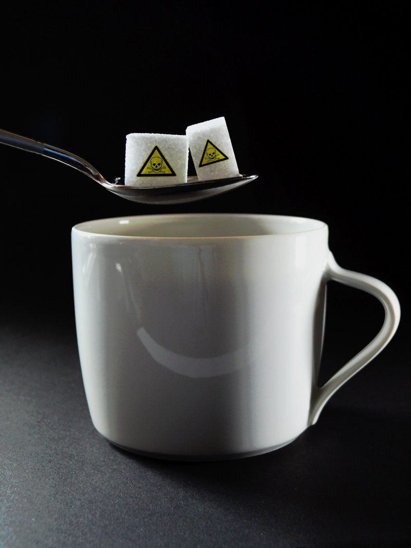 Two sugar cubes with poison hazard stickers, held on a spoon over coffee mug